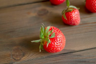 Tahta bir masada olgun çilekler. Masada yeşil kuyruklu çilekler. Çilek mevsimi - böğürtlenler masaya serildi.