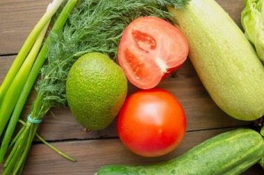 Tahta bir masada sağlıklı sebzeler vardır. Sağlık için yeşil ve kırmızı sebzeler. Salata için domates, lahana, kabak, salatalık ve avokado..