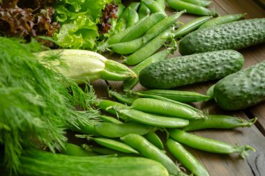 Salatalık, marul ve dereotu, yeşil bezelye, lahana ve kabak yan yana yatar. Tahta bir masada bir sürü bahar sebzesi ve otlar var..