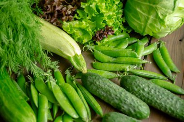 Salatalık, marul ve dereotu, yeşil bezelye, lahana ve kabak yan yana yatar. Tahta bir masada bir sürü bahar sebzesi ve otlar var..