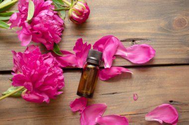 Şakayık yağı. Bir şişe temel yağ şakayık çiçeklerinin yanındaki ahşap bir masanın üzerinde yatıyor. Şakayığın çiçek ve yaprakları arasında bir şişe gerekli yağ yatıyor..