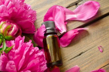 Şakayık yağı. Bir şişe temel yağ şakayık çiçeklerinin yanındaki ahşap bir masanın üzerinde yatıyor. Şakayığın çiçek ve yaprakları arasında bir şişe gerekli yağ yatıyor..