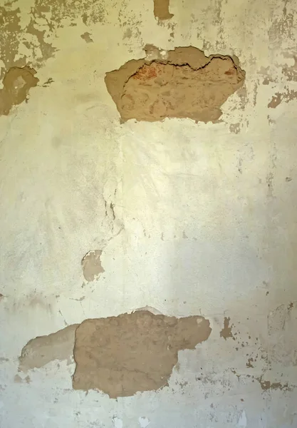An old wall with crumbling plaster. Plaster is crumbling on the wall. The wall needs repair.