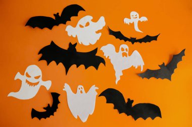 Turuncu arka planda kağıttan yapılmış hayaletler ve yarasalar. Parlak turuncu arka planda, cadılar bayramı el sanatları. Çocuklar için Cadılar Bayramı süslemeleri - hayaletler ve yarasalar.