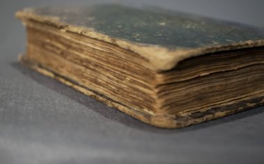 Dayak yemiş bir kitap. Eski bir kitap gri bir arka planda yatıyor. Çok eski bir yakın çekim kitabı..