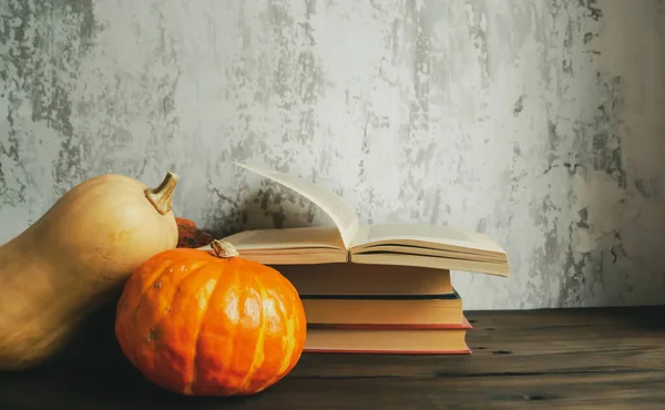 Autumn arrangement of pumpkin and books against grey wall. Books next to pumpkins.