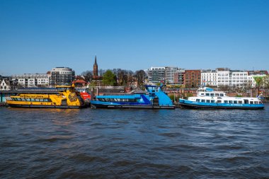 Hamburg, Almanya - 04 17 2023: Hamburg 'da nehir elbindeki bir rıhtımda 3 demirli feribotta arka planda evleri olan sudan manzara.