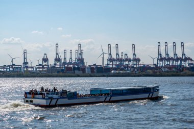 Hamburg, Almanya - 04 17 2023: turistler Hamburg limanında ışığa ve arka plandaki vinç ve konteynırlara karşı mavna yolculuğu yapıyorlar