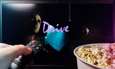 Kyiv. Ukrayna. 11.12.2023: Drive filmini patlamış mısır ve uzaktan kumandayla izleyen kişi. Stok editör fotoğrafı.