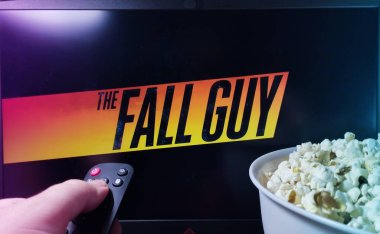 Kyiv. Ukrayna. 10.11.2023: The Fall Guy 'ı televizyonda patlamış mısır ve uzaktan kumandayla izleyen kişi. Stok editör fotoğrafı.