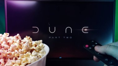 Kyiv. Ukrayna. 10.11.2023: Patlamış mısır ve uzaktan kumandalı Dune Part Two filmi izleyen kişi. Stok editör fotoğrafı.