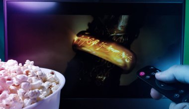 Kyiv. Ukrayna. 10.11.2023: Televizyonda patlamış mısır ve uzaktan kumandayla Yüzüklerin Efendisi 'ni izleyen kişi. Ekrandaki Tek Yüzük. Stok editör fotoğrafı.