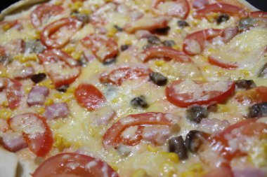 Katmanlar halinde peynir, dilimlenmiş domates, mantar, mısır ve jambondan oluşan ev yapımı bir pizza fırından canlı renkler ve lezzetli malzemeler sunar..