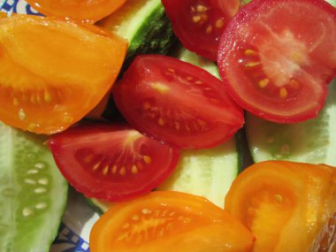 Parlak kırmızı ve turuncu domates dilimleri tabakta gevrek salatalık parçaları ile karıştırılır. Tazeliklerini ve davetkar renklerini vurgularlar. Yaz salatası için mükemmeldir..