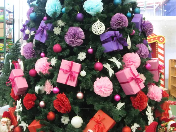 Güzel dekore edilmiş bir Noel ağacı canlı süsler, renkli hediye kutuları ve mevsimlik dekorasyonlar içerir, şenlikli bir iç mekanda neşeli bir atmosfer yaratır..