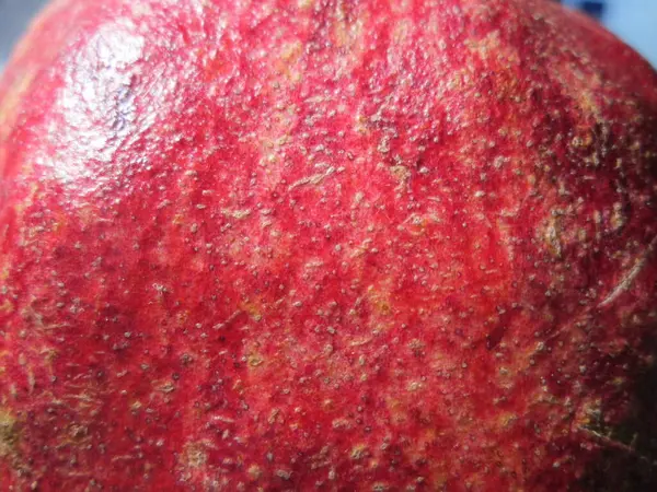 stock image The pomegranate features a striking red surface with intricate texturing, reflecting the sunlight and emphasizing its ripe, fresh quality as seen in a local market setting.