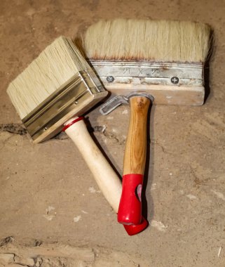 Biri ahşap saplı, diğeri de kırmızı plastik saplı olmak üzere iki boya fırçası dokulu bir yüzeye yerleştiriliyor. Aletlere bakılırsa usta bir işçilik..