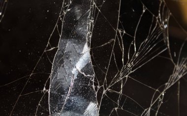 Yakından bakınca, karanlık bir arkaplan üzerine kurulu, karmaşık desenleri ve yansımaları olan kırık bir cam yüzeyi ortaya çıkarıyor..