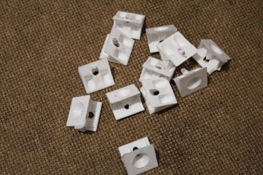 Çuval bezi benzeri bir dokuda küçük, beyaz plastik kliplerin bir koleksiyonu sergilenerek, bunların pratik tasarımı ve öğeleri düzenlemek için çok yönlülüğü vurgulanıyor.