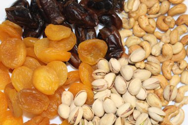 Beyaz bir yüzeye dizilmiş çeşitli kurutulmuş kayısılar, hurmalar, kaju fıstıkları ve fıstıklar besin değeri yüksek abur cuburların zengin renklerini ve dokularını ön plana çıkarırlar..