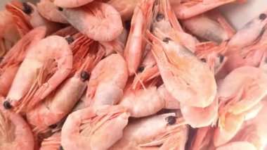 Yakından bakınca sayısız donmuş pembe karidesin üst üste yığıldığını görüyoruz. Karides satılığa ya da hazırlığa hazır görünüyor. Renkleri ve dokuları donmuş olduklarını gösteriyor..