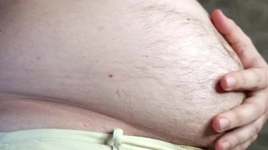 Adam koca karnını muayene ediyor. Oturma işi sırasında vücut pozitifliği ve kilo alma kavramı. Erkek karnının dolu olduğu stok videosu..