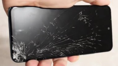 Bir el, ciddi şekilde çatlamış bir ekranla akıllı telefonu kavrarken görülüyor..