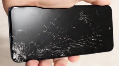 Bir el, ciddi şekilde çatlamış bir ekranla akıllı telefonu kavrarken görülüyor.. 