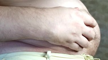 Koca göbeğini elinde tutan bir adam. Aşırı yemek yeme ve obezite kavramı. Stok videosu.