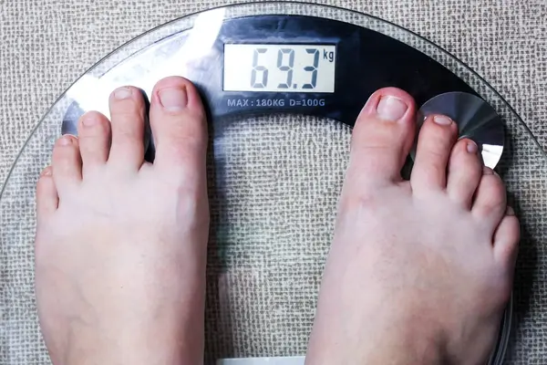 Çıplak ayaklar, şeffaf cam bir ölçekte vücut ağırlığını gösterir. Sağlık ve sağlık odaklanması.