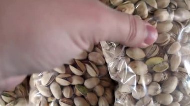 Bir el taze fıstıkla dolu çantaları inceler, canlı renkleri ve dokuları sergilenir. Kurulum, bu cevizlerin müşteriler için satıldığı yerel bir pazar gibi görünüyor. Yakın çekim.