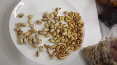 Bir el, tabakta çeşitli fındıkları ustalıkla ayırıp sağlıklı bir atıştırmalık için mükemmel parçaları seçiyor. Çeşit çeşit ceviz, fıstık ve diğer lezzetli seçenekleri içeriyor. Bu kadar basit