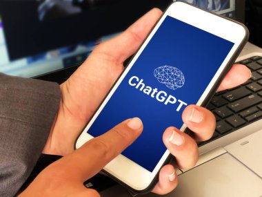 Man using ChatGPT on Mobile with blue background and laptop in the backdrop. Modern ai writing tool using concept editorial wallpaper