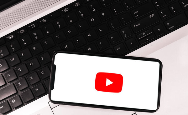 Видеопотоковая платформа youtube на мобильном экране с ноутбуком в фоновом режиме, редакционная