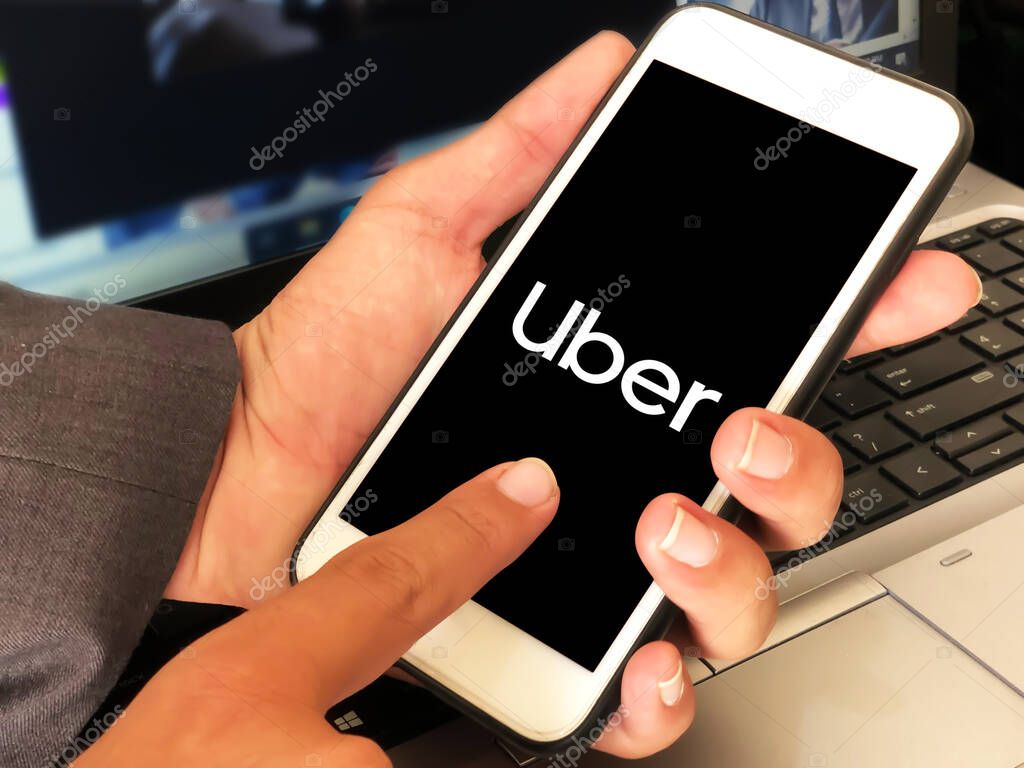 Man using ride hailing service uber on mobile with laptop in the backdrop, editorial