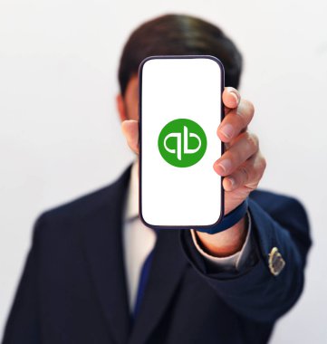 Akıllı telefon ekranında QuickBooks 'un mobil uygulamasını gösteren kişi, teknik arkaplan