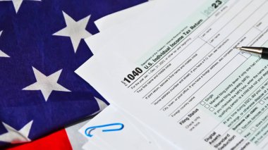 ABD Gelir İade Belgesi 1040 formu. Arka planda ABD bayrağı var. Kağıt tarafında da yer var. Kalem ve bayrak arkaplanlı vergi formu doldurma kavramı