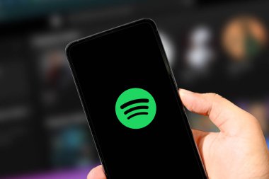 3.23.2025, Birleşik Devletler. Kişi, akıllı telefondaki müzik akışı uygulamasını kullanarak yakın plan, illüstrasyonal arka plan