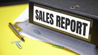 Satış Raporu tipografisi siyah dosya makasının yanında yazılıydı. Kağıt üzerinde sarı masa ve kalem vardı. 4k görüntü kapatıldı.