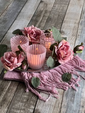 Ahşap bir masanın üzerinde mumlar ve güllerle pembe cam şamdanlar. Kart. Fotoğraf.