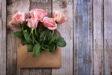 Tahta bir masanın üzerinde kağıt bir zarfın içinde pembe güller. Yaratıcı bir hediye. Kart. Uzayı kopyala Fotoğraf.