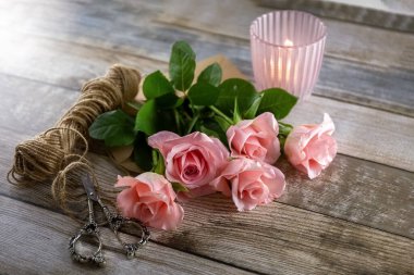 Pink roses, a spool of thread, scissors and a candlestick on a wooden table. Postcard. Photo