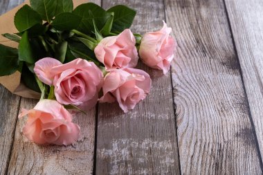 Tahta bir masanın üzerinde kağıt bir zarfın içinde pembe güller. Yaratıcı bir hediye. Uzayı kopyala Fotoğraf.