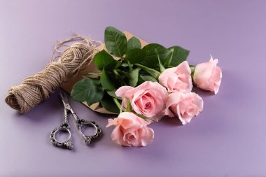 Pink roses, a spool of thread, scissors and a candlestick on a purple table. Postcard. Photo