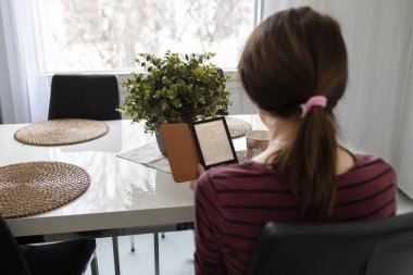 Bir kadın sırtı dönük bir şekilde bir masada oturuyor ve elektronik kitap okuyor. Fotoğraf.