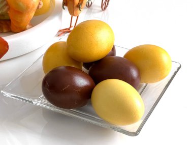 Sarı ve kahverengi Paskalya yumurtaları bir tabakta, beyaz bir masada. Fotoğraf.