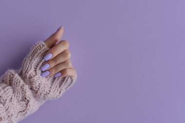 Dini manikürlü bir kadın eli. Mor arkaplanda modaya uygun lavanta rengi tırnakları, kopyalama alanı 