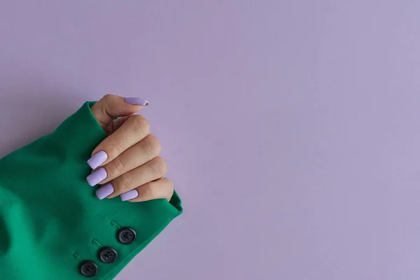 Female's hand with purple nails wearing green jacket on purple background. Gelish manicure