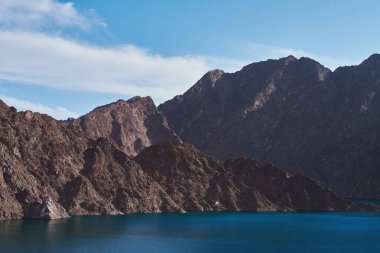 Hatta Baraj Peyzajı. Açık mavi suları ve gündüz vakti Hajar dağları olan bir göl. Dubai Meclisi