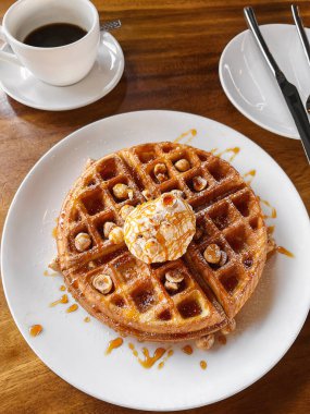 Kahveyle servis edilen bir top dondurma, fındık ve karamel şurubuyla bir yığın waffle. Bir kafede kahvaltı yapmak. Rahatlatıcı gıda konsepti
